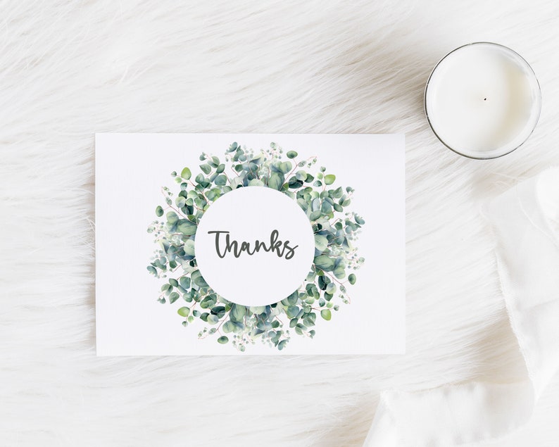 May include: A white card with a green eucalyptus wreath around a circle that says "Thanks" in black script.
