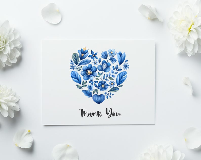 May include: A white greeting card with a blue floral heart design and the words "Thank You" in black script. White flowers and petals surround the card on a white background.