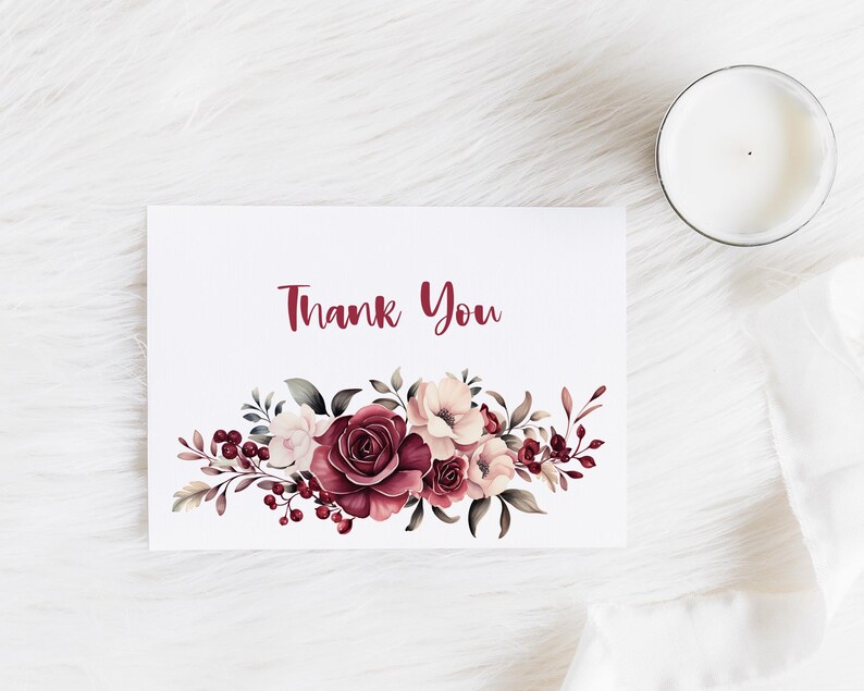 May include: A white card with the words "Thank You" in burgundy script. The card features a watercolor floral design in shades of burgundy, pink, and cream. A lit candle in a glass jar sits to the right.