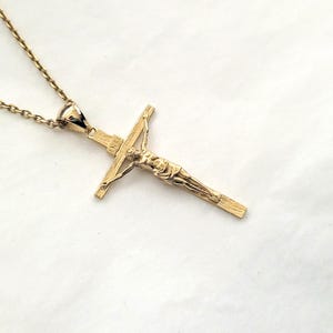 May include: A gold chain necklace with a gold crucifix pendant. The crucifix features a detailed depiction of Jesus Christ.
