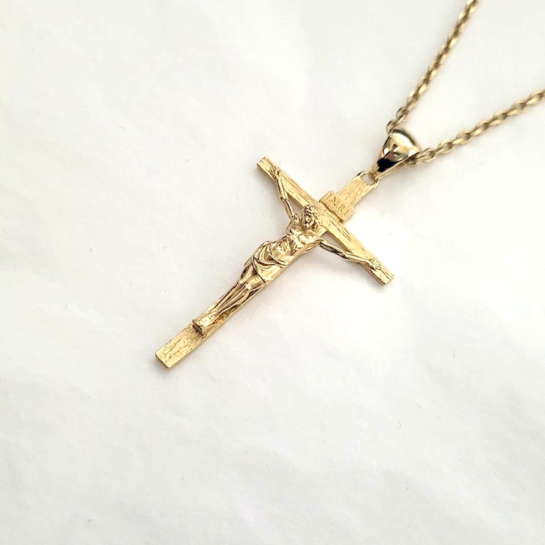 May include: A gold-toned pendant necklace featuring a detailed crucifix with a figure of Jesus Christ. The chain is a delicate rope style.