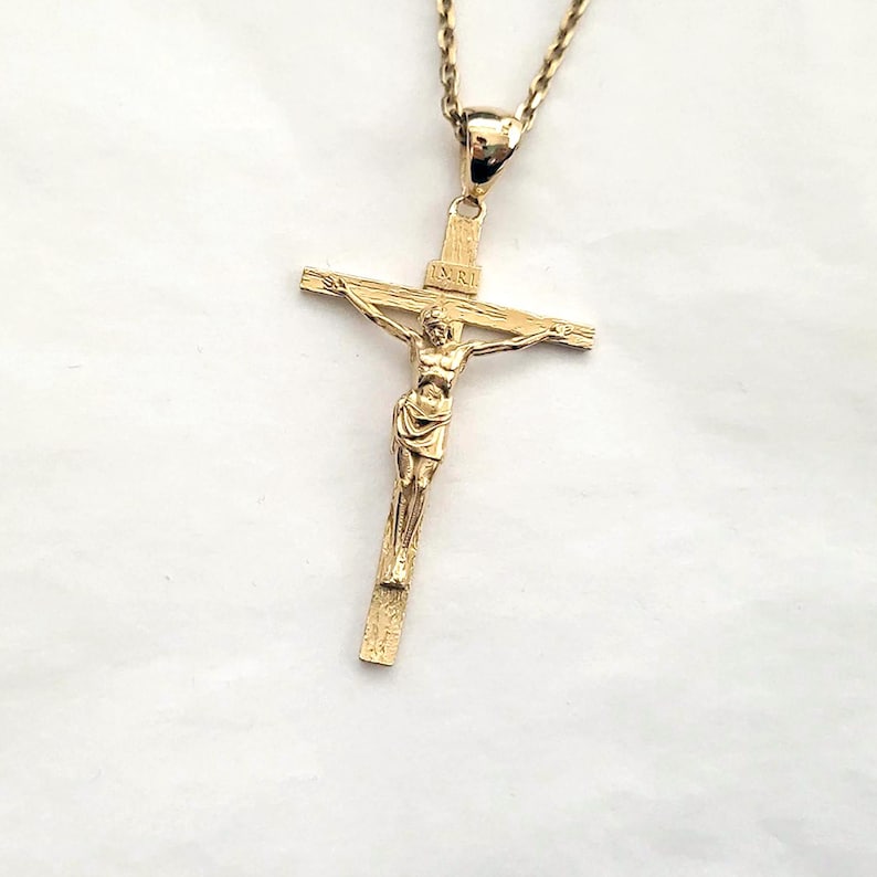 May include: A gold-toned crucifix pendant with a detailed figure of Jesus Christ. The pendant is attached to a gold chain.
