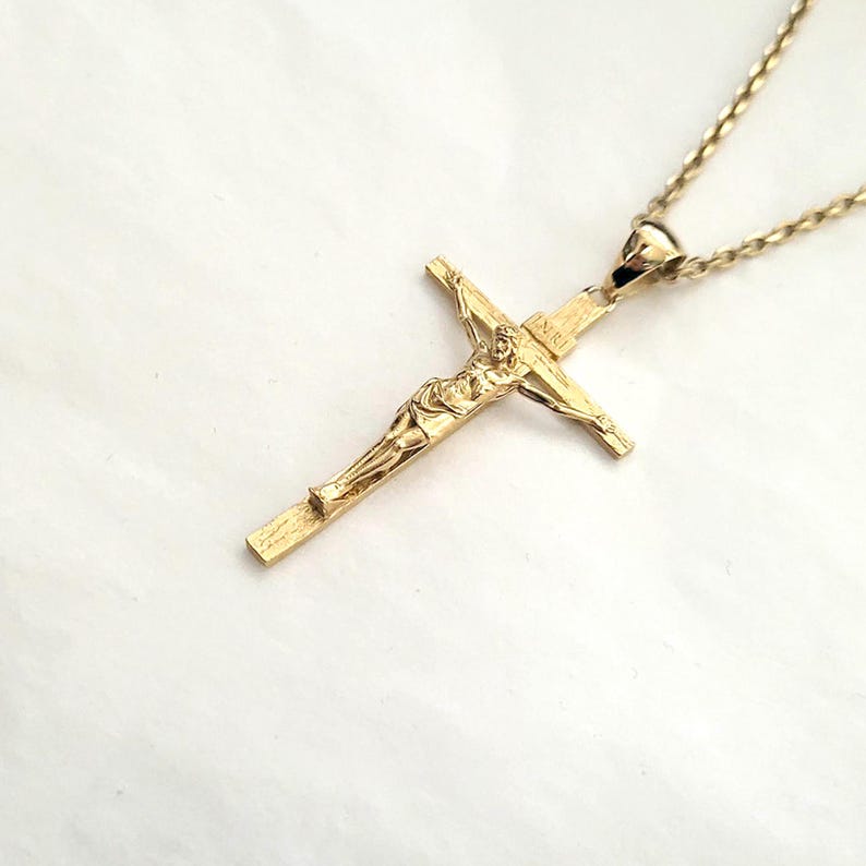 May include: A gold chain necklace with a detailed gold crucifix pendant.