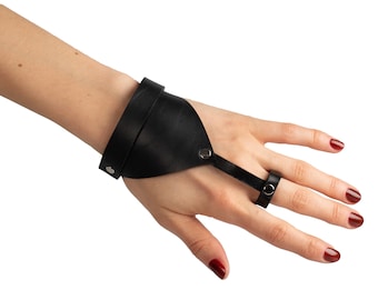 May include: Black leather fingerless glove with a strap that goes around the wrist and a ring that goes around the middle finger.