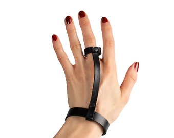 May include: A black leather finger ring and bracelet with a snap closure. The ring is adjustable and the bracelet is worn on the wrist.