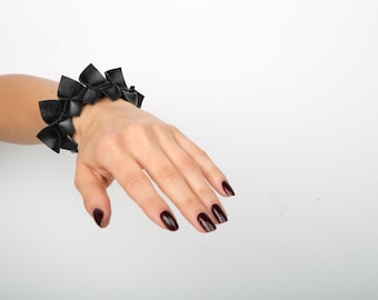 Puede incluir: Un brazalete de cuero negro con un diseño geométrico único. El brazalete está hecho de múltiples piezas de cuero superpuestas, creando un aspecto texturizado y llamativo.