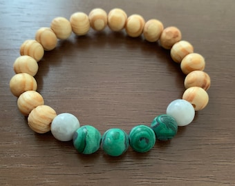 May include: A wooden bead bracelet with green and white beads. The bracelet is made of natural wood and has a simple design.