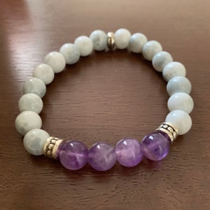 May include: A bracelet made of light blue and purple beads. The bracelet has silver accents and is made of natural stones.