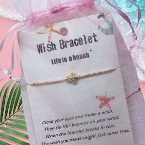 May include: A pink and gold wish bracelet with a small gold turtle charm. The bracelet is packaged in a pink organza bag. The card reads "Wish Bracelet" and "Life is a beach". The card also includes instructions on how to make a wish and tie the bracelet.