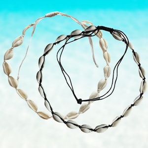 Peut inclure: Deux colliers de coquillages, un blanc et un noir, sur un fond bleu.