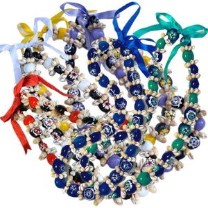 May include: A set of six colourful shell leis with blue, green, red, yellow, and purple accents. The leis are made of natural shells and feature hand-painted floral designs.