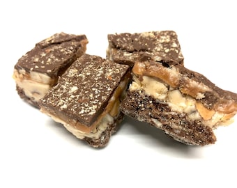 May include: Four chocolate-covered squares of fudge with a layer of caramel and nuts. The fudge is topped with a sprinkle of chopped nuts.