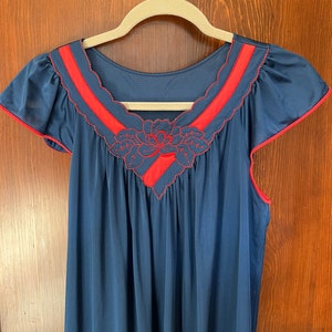May include: A navy blue nightgown with red trim and a floral embroidery design on the neckline.