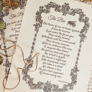 May include: Two cream-coloured prints featuring the poem "The Bee" by Emily Dickinson, with ornate black borders and bee illustrations. The text is in a classic serif font. A length of twine rests on the prints, suggesting a rustic theme.