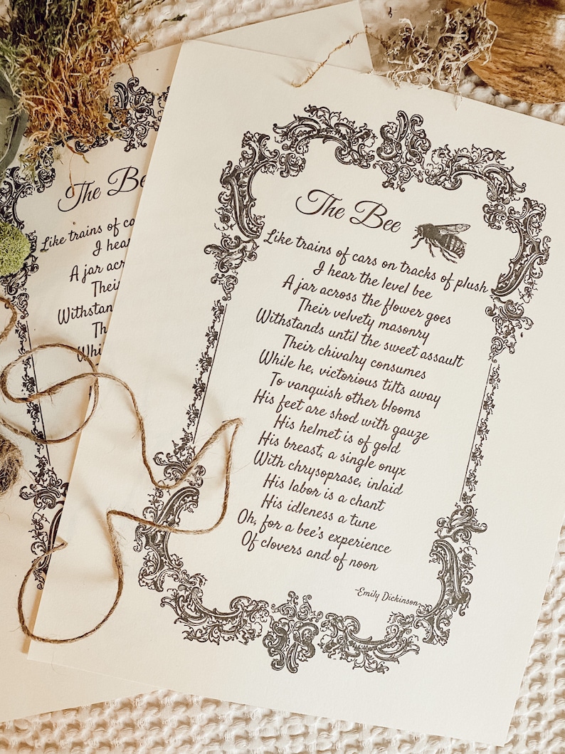 May include: Two cream-coloured prints featuring the poem "The Bee" by Emily Dickinson, with ornate black borders and bee illustrations. The text is in a classic serif font. A length of twine rests on the prints, suggesting a rustic theme.