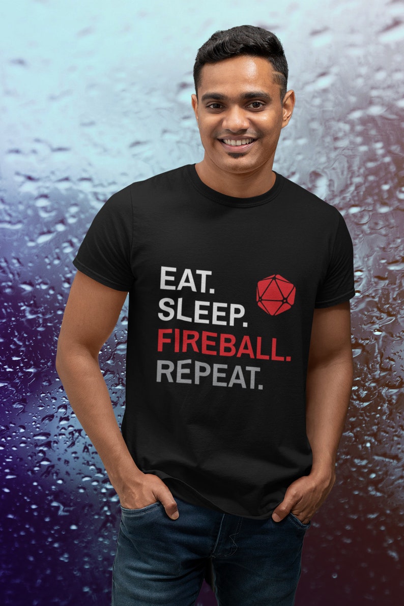Może przedstawiać: Czarny t-shirt z napisem "EAT. SLEEP. FIREBALL. REPEAT." w kolorze białym i czerwonym oraz czerwonym geometrycznym kształtem. Koszulka jest noszona przez osobę w niebieskich dżinsach.