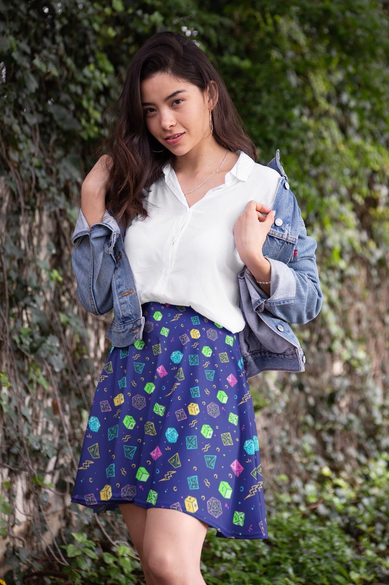 May include: A woman wearing a white button-down shirt, a blue denim jacket, and a blue skirt with a colorful dice pattern.