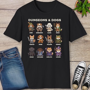 May include: Black t-shirt featuring the text "DUNGEONS & DOGS" above cartoon dog illustrations representing various fantasy classes like Bard, Barbarian, and Rogue. The shirt is paired with blue jeans and black sneakers.
