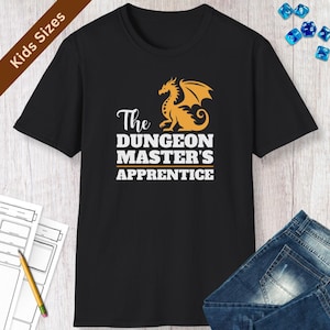 May include: Black t-shirt with the text "The Dungeon Master's Apprentice" in white, and an orange dragon graphic. The words "Kids Sizes" are printed on a brown banner in the upper left corner.