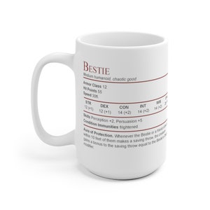 May include: White ceramic mug with a brown outline and text that reads "BESTIE" and includes character stats for a Dungeons and Dragons character. The text includes "Medium humanoid, chaotic good", "Armor Class 12", "Hit Points 55", "Speed 30ft.", "STR 12 (+1)", "DEX 12 (+1)", "CON 14 (+2)", "INT 14 (+2)", "WIS 14 (+2)", "Skills Perception +2, Persuasion +5", "Condition Immunities frightened", "Aura of Protection. Whenever the Bestie or a friend of theirs within 10 feet of them makes a saving throw, the creature gains a bonus to the saving throw equal to the Bestie's modifier."