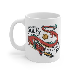 May include: White ceramic mug with a red dragon illustration and the text "When the DM smiles it's already too late".