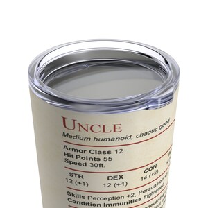 May include: A stainless steel tumbler with a clear plastic lid. The tumbler has a cream-colored background with red text that reads "UNCLE" and other game statistics. The tumbler is designed for hot or cold beverages.