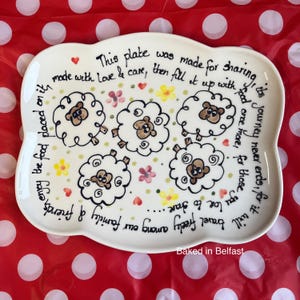 May include: A decorative white ceramic serving plate with a sheep design and handwritten text. The plate features five sheep illustrations, flowers, and the text: "This plate was made for sharing." The words "Baked in Belfast" are also included.