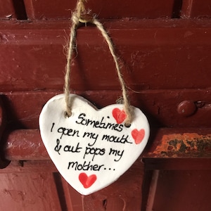 May include: White heart-shaped ceramic ornament with red hearts and the text "Sometimes I open my mouth & out pops my mother..." hanging from a string.