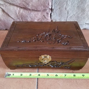 May include: A wooden jewelry box with a carved scene of a city on the lid. The box has a brass latch and is approximately 8 inches long.