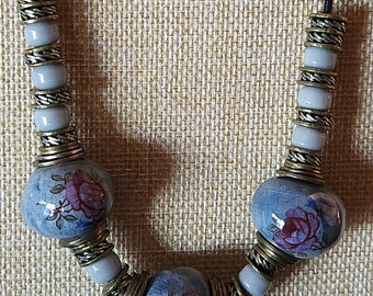 May include: A necklace with blue and white ceramic beads with floral designs and gold accents.