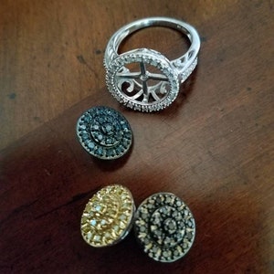 May include: A set of three silver rings with diamond accents. The rings are in a circular shape and have a delicate design. The rings are on a wooden surface.