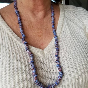 May include: A necklace made of blue and brown glass beads with a white pattern. The beads are cylindrical and have a slightly irregular shape.
