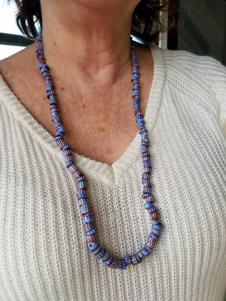 May include: A necklace made of blue and brown glass beads with a white pattern. The beads are cylindrical and have a slightly irregular shape.