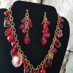 May include: A red and gold necklace and earrings set with a chain link design and red glass beads. The necklace has two cameo pendants with floral designs.