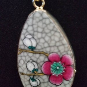 May include: A white ceramic pendant with a crackled glaze features a pink flower with a green center and white flowers with green leaves on gold stems.