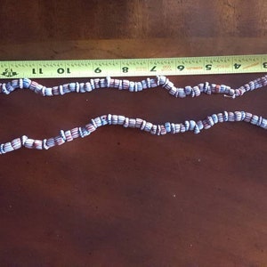 May include: A necklace made of blue and red striped beads. The necklace is approximately 11 inches long.