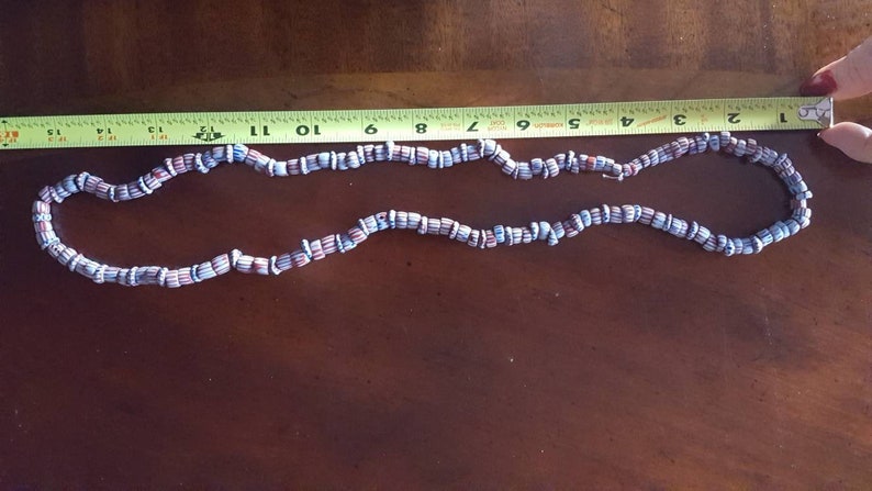 May include: A necklace made of blue and red striped beads. The necklace is approximately 11 inches long.