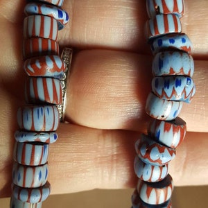 May include: A close-up of a strand of blue and red glass beads. The beads have a white and red striped pattern and a blue and white floral pattern.