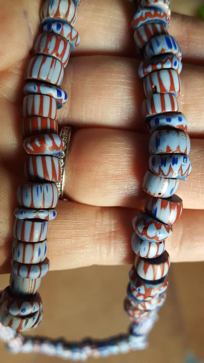 May include: A close-up of a strand of blue and red glass beads. The beads have a white and red striped pattern and a blue and white floral pattern.