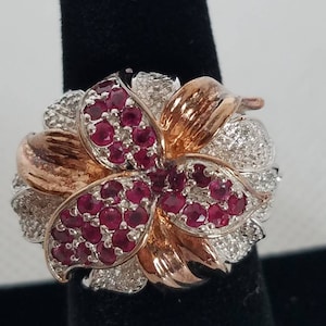May include: A silver and rose gold ring with a flower design. The flower is made of small red gemstones and white diamonds.