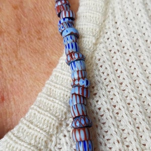 May include: A close-up of a necklace made of blue and red glass beads. The beads are patterned with stripes and dots.