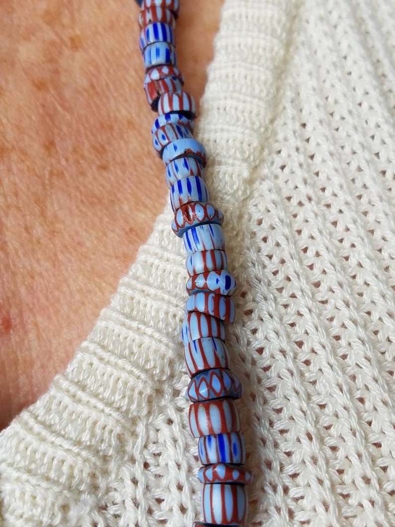 May include: A close-up of a necklace made of blue and red glass beads. The beads are patterned with stripes and dots.