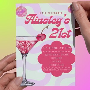 Puede incluir: Tarjeta de invitación rosa y blanca con el texto "Let's Celebrate Ainsley's 21st". Presenta una ilustración de cóctel con una cereza, bolas de discoteca y detalles del evento: fecha, hora, dirección y contacto RSVP.