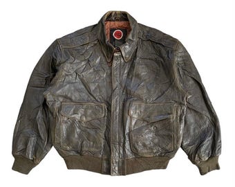May include: A brown leather bomber jacket with a zip fastening and two large pockets. The jacket has a distressed look and a red circular logo on the left side of the chest.