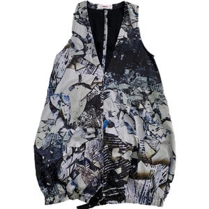 Pode incluir: Top sem mangas com decote em V e um padrão abstrato único. O design apresenta uma mistura de formas brancas, pretas e azuis. A bainha inferior é franzida e um pequeno detalhe de fivela preta é visível. O top é feito de tecido leve.