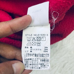 May include: Close-up of a red fabric with a white tag attached. The tag displays washing instructions and fabric composition details, including 74% cotton and 26% polyester. The style number is 6153513.