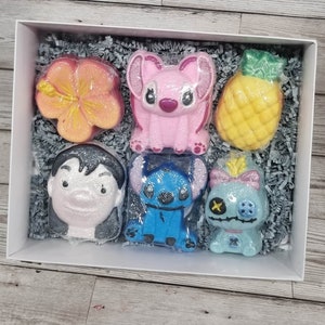 May include: A set of six bath bombs in a white box with grey shredded paper. The bath bombs are shaped like a pineapple, a hibiscus flower, Stitch, Lilo, and two other Stitch characters.