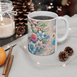 Könnte beinhalten: Eine weiße Keramiktasse mit einem rosa-blauen Blumendesign. Die Tasse ist mit Kaffee oder Tee gefüllt und Dampf steigt aus der Oberseite auf.