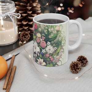 Könnte beinhalten: Eine weiße Keramiktasse mit einem Blumendesign mit rosa, weißen und grünen Blumen. Die Tasse ist mit Kaffee oder Tee gefüllt und Dampf steigt aus der Oberseite auf.