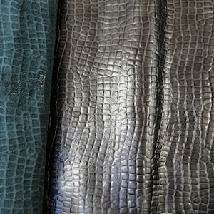 May include: Close-up of two pieces of dark brown leather with a crocodile embossed pattern. The leather is folded in half, showing the texture and sheen.